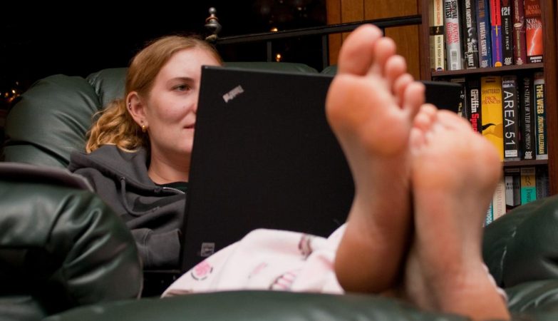 Jovem descalça no sofá acede à internet num computador portátil Lenovo