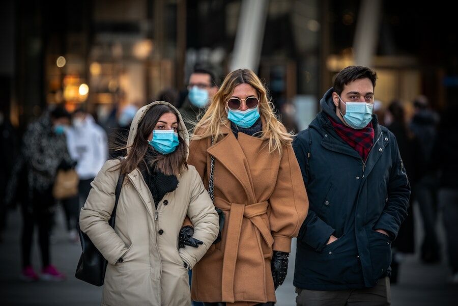 Três pessoas – duas mulheres e um homem – a passear na rua com máscara