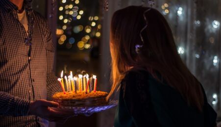 Um homem a segurar num bolo de aniversário enquanto uma jovem sopra as velas