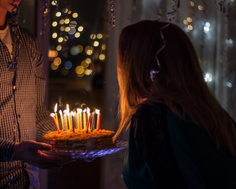 Um homem a segurar num bolo de aniversário enquanto uma jovem sopra as velas