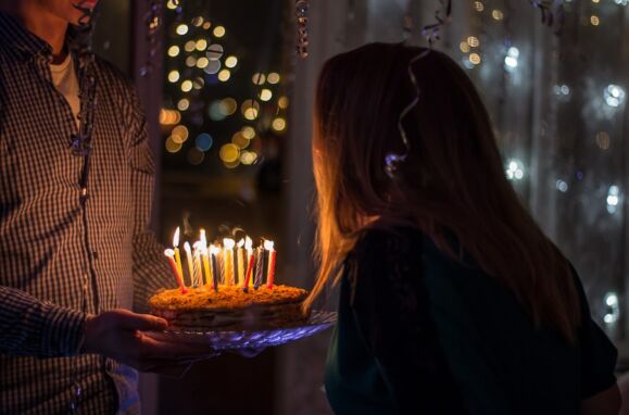 Um homem a segurar num bolo de aniversário enquanto uma jovem sopra as velas