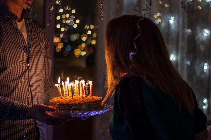Um homem a segurar num bolo de aniversário enquanto uma jovem sopra as velas