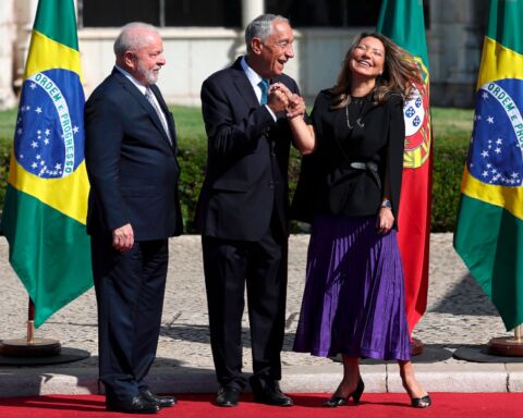 Marcelo Rebelo de Sousa segura na mão de Janja enquanto ela sorri, com a cabeça inclinada para trás e os olhos fechados, e Lula da Silva observa ao lado.