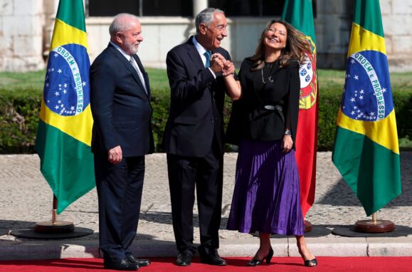 Marcelo Rebelo de Sousa segura na mão de Janja enquanto ela sorri, com a cabeça inclinada para trás e os olhos fechados, e Lula da Silva observa ao lado.