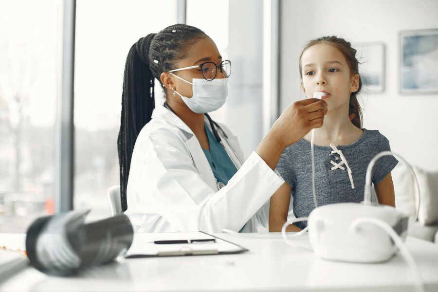Médica de óculos e de máscara analisa criança com asma.