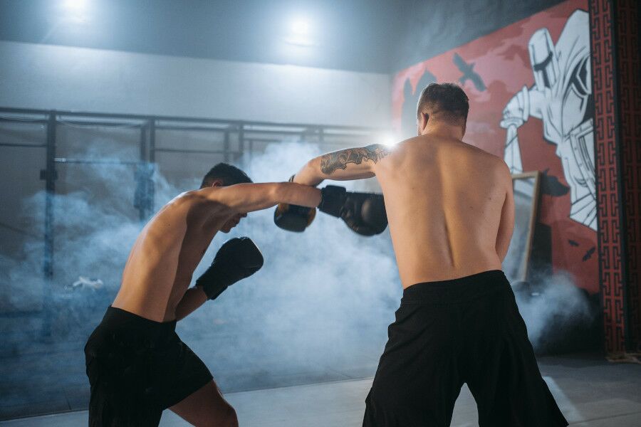 Lutadores de MMA - Artes Marciais mistas de calções pretos, sem camisola, e luvas de boxe a treinar.