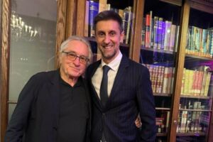 O actor Robert De Niro e o diretor de programas da SIC Daniel Oliveira lado a lado em frente a uma estante de livros.