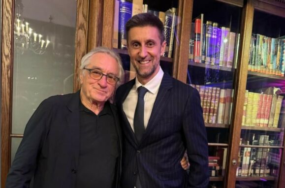 O actor Robert De Niro e o diretor de programas da SIC Daniel Oliveira lado a lado em frente a uma estante de livros.