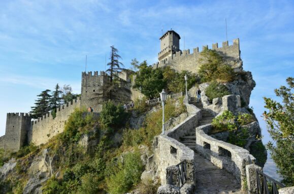 Paisagem em São Marino com castelo e muralhas no topo de montanha.