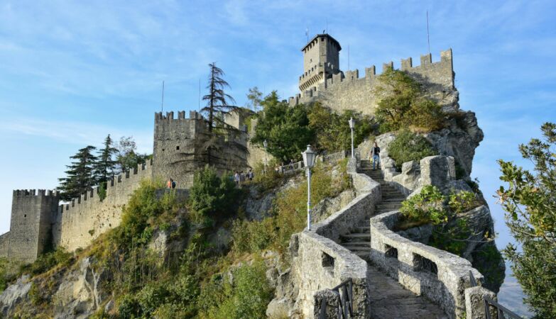 Paisagem em São Marino com castelo e muralhas no topo de montanha.