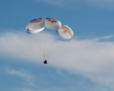 Cápsula da SpaceX com paraquedas no céu azul, no regresso à Terra dos astronautas da NASA presos no espaço.