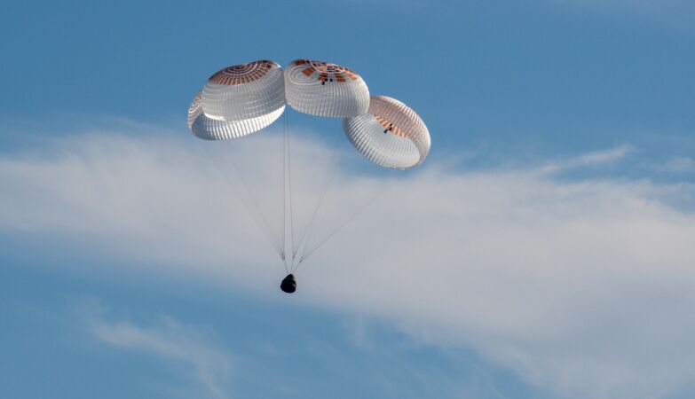 Cápsula da SpaceX com paraquedas no céu azul, no regresso à Terra dos astronautas da NASA presos no espaço.