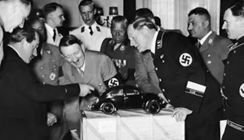 Ferdinand Porsche revela o conceito Volkwagen na presença de um Adolf Hitler visivelmente entusiasmado, ao descobrir que o motor se situa na mala do carro.